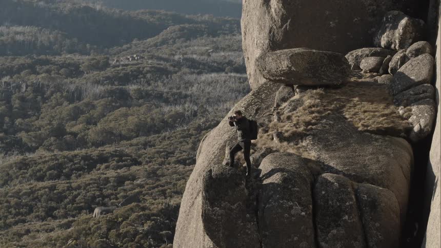 A man standing on a cliff taking pictures with his camera