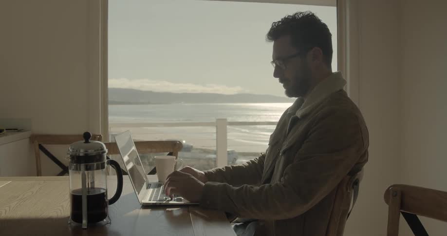 A man works on a lap top with coffee on the table beside him
