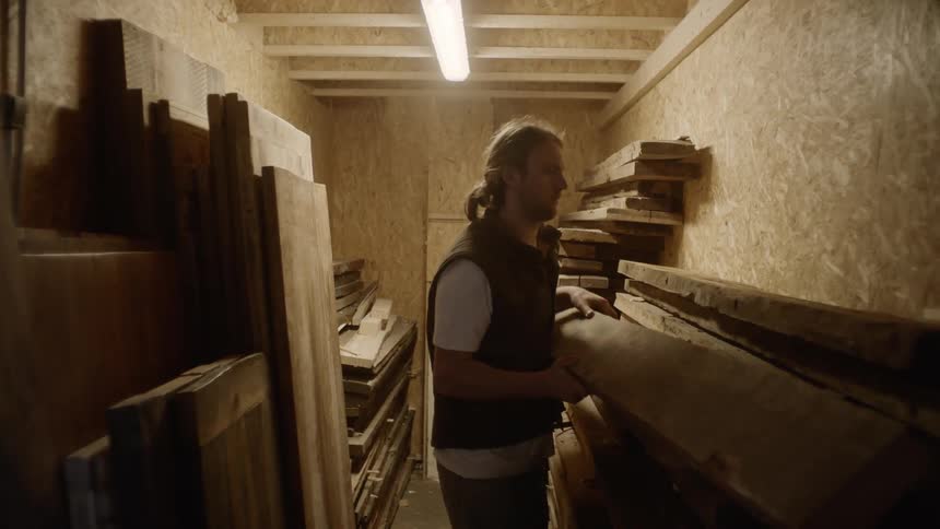 A man is stacking planks of wood in a shed