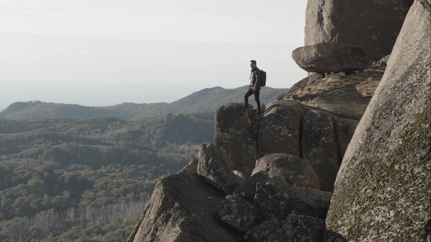 A male caucasian hiking onto a cliff in the mountains