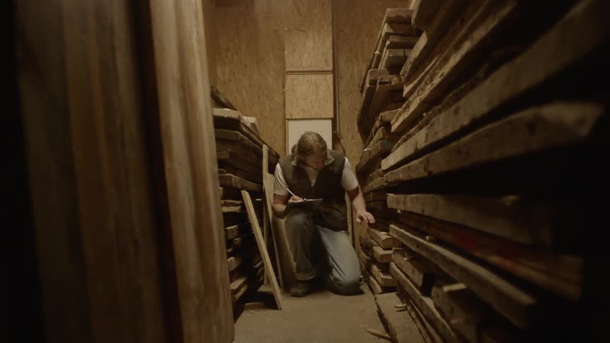 Man kneels between two piles of sawn timber and counts them by taking notes indoors