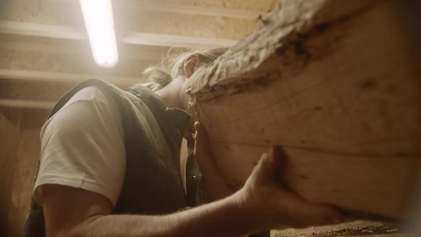 Male inspecting piece of lumbar off a stack of wood in a room
