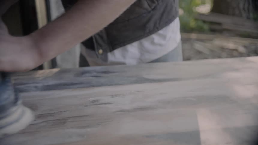 A caucasian male sanding wood outside