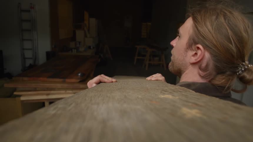 A white caucasian carrying a wood plank from outside to a workshop