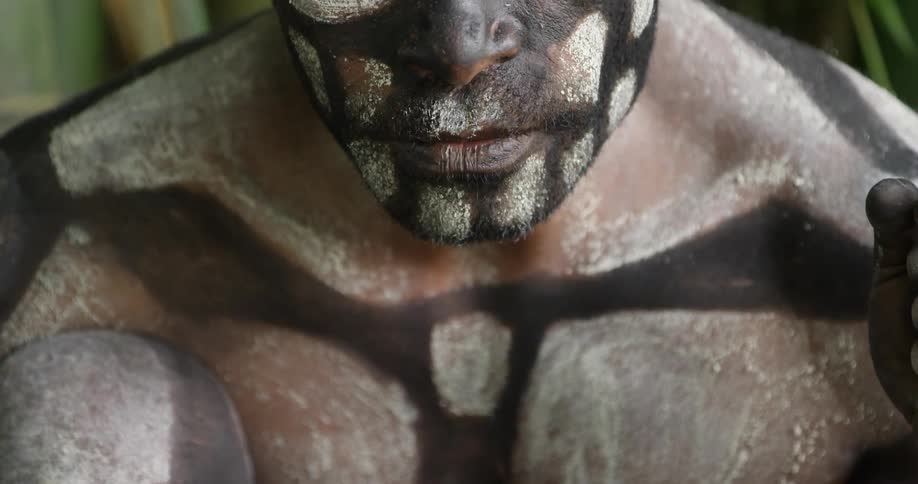 A man covered with body paint sits unmoving