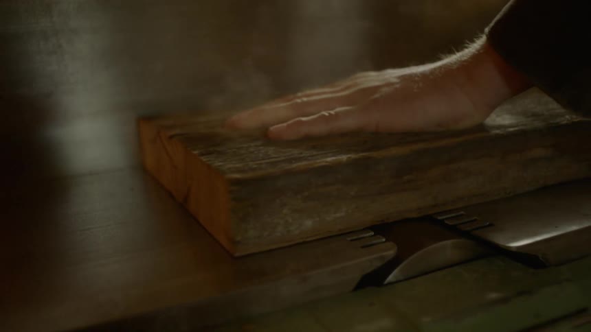 A person that is running a piece of wood across a saw blade