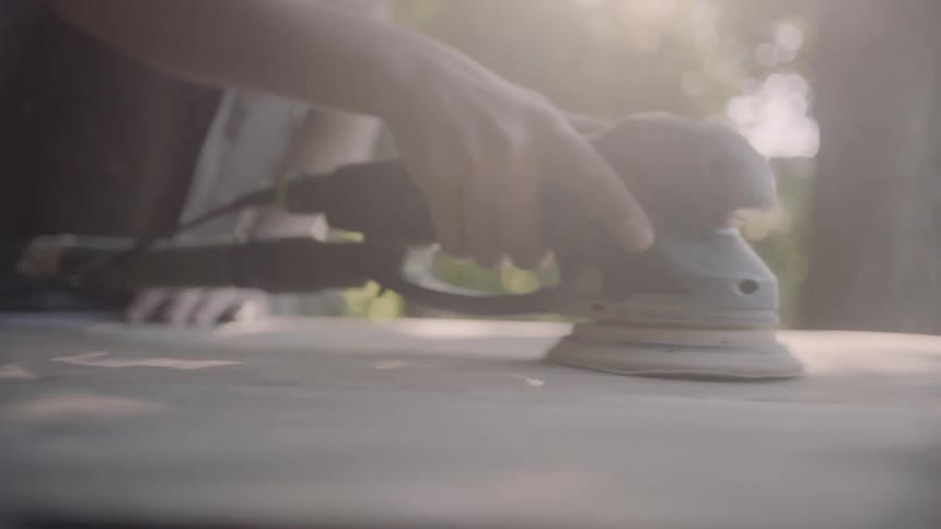 A person with an electric sander sanding a piece of wood