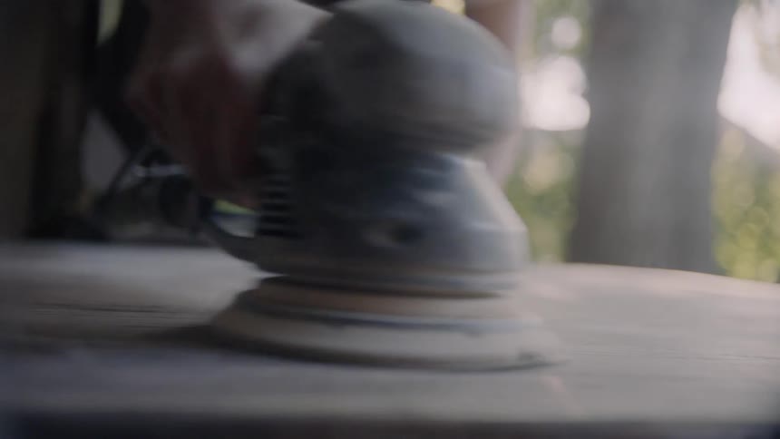 A person sanding a piece of wood outdoors