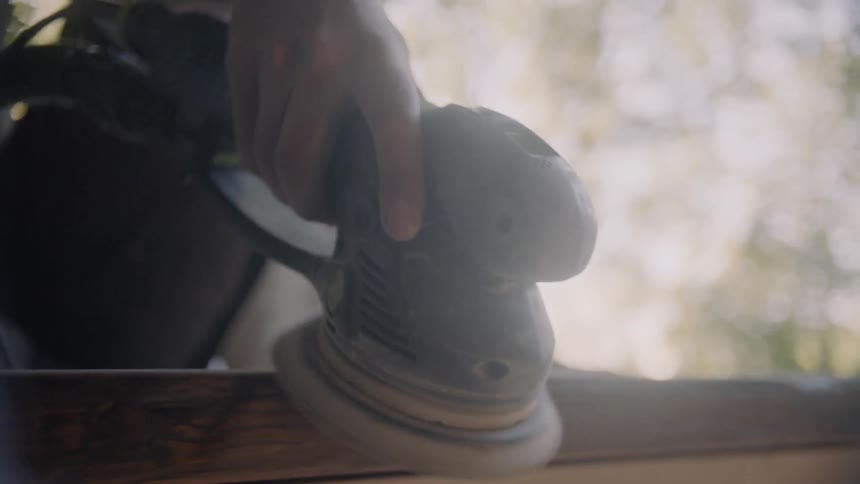 A man uses a sander on a piece of wood