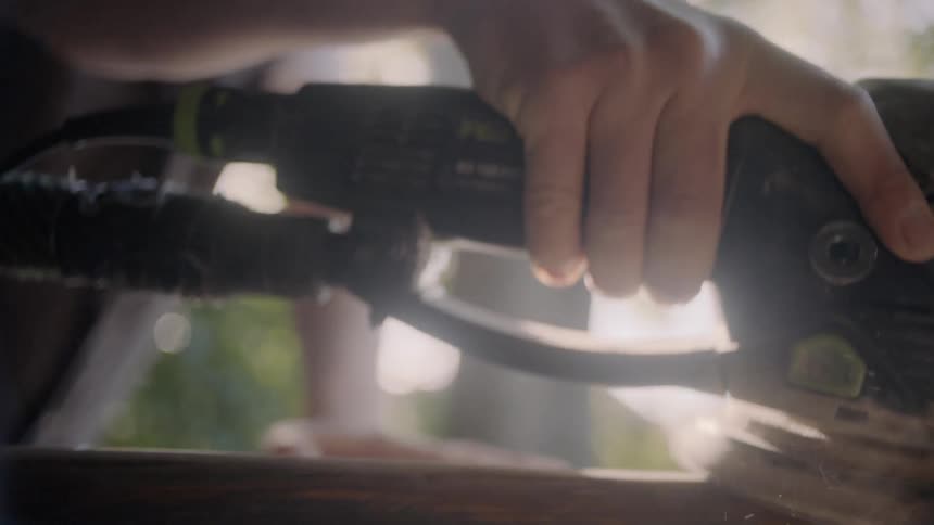 A man sands down a piece of wood in daylight