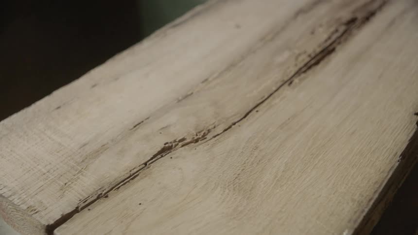 A flat piece of wood is stationary and amidst the wood grain is a single dark crack down the lenght of the wood in its center