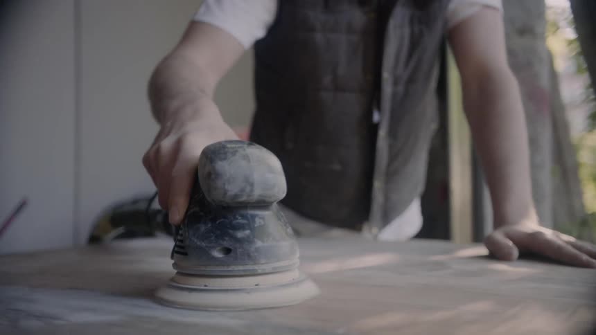 A man sanding a large slab of wood with an electric sander