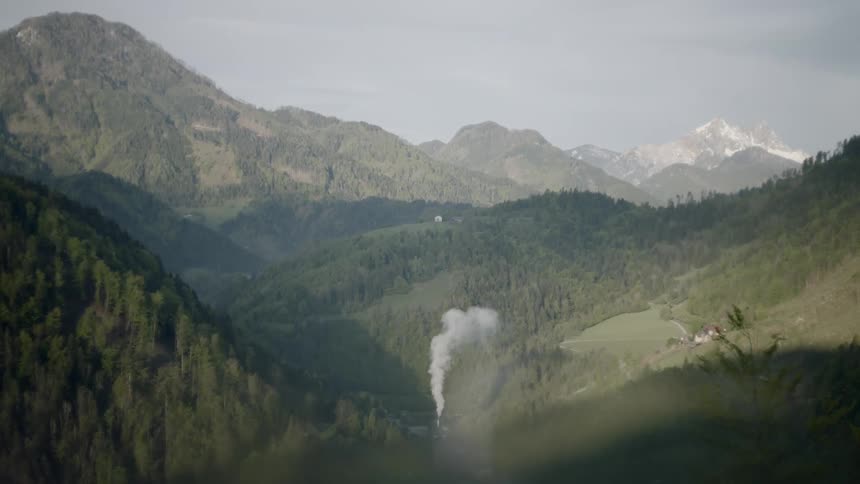 A chimney with smoke coming out of it with mountains in the background