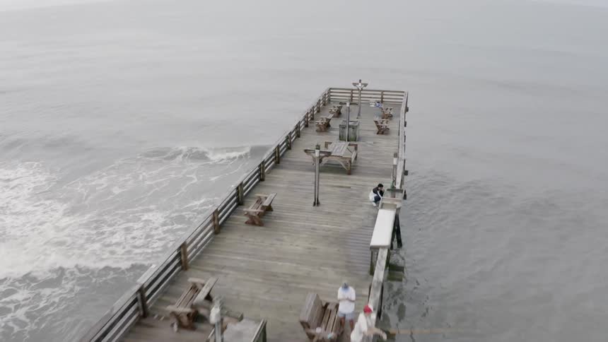 A wooden pier furnished with benches extends out into sea in daylight