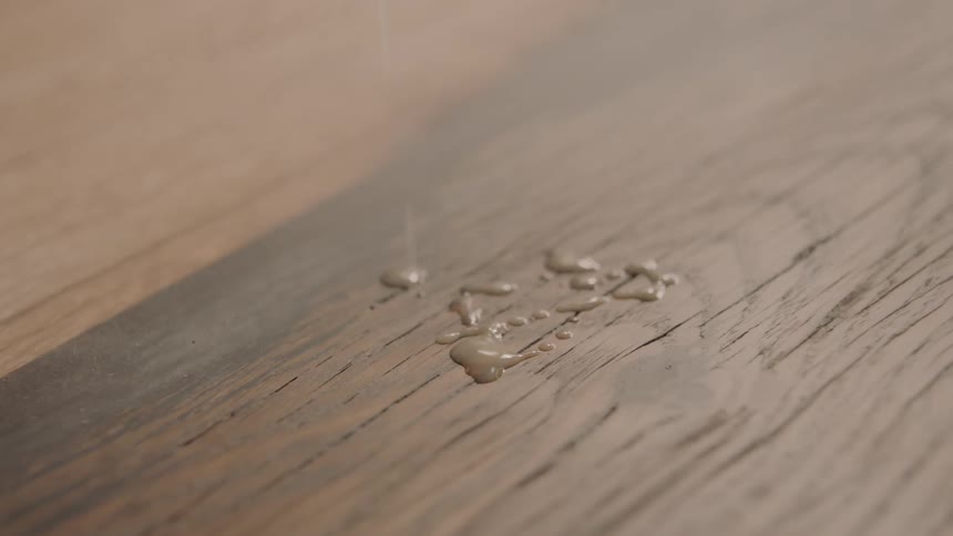 An opaque tan liquid is slowly dripped onto a fine wooden surface