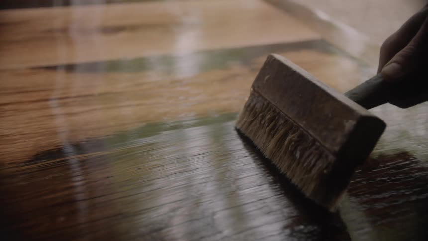A person using a brush to apply finish to a wood surface