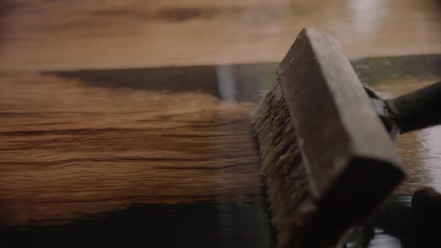 A person smoothing a wax like substance on a wooden surface with a brush
