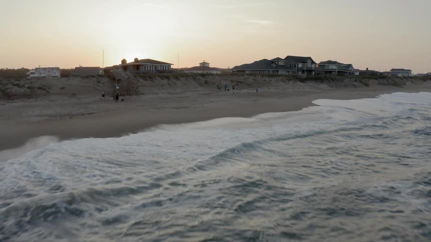 Aerial view of waves into the beach and homes set behind the sand dunes at sunset