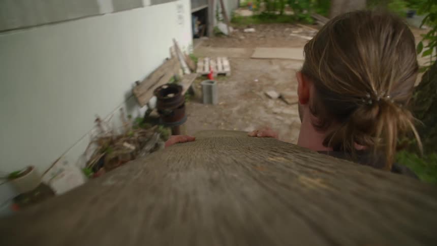 A person carrying a piece of wood outside