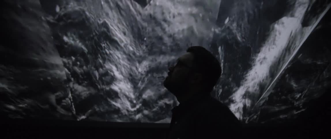 A man with glasses standing underneath a screen