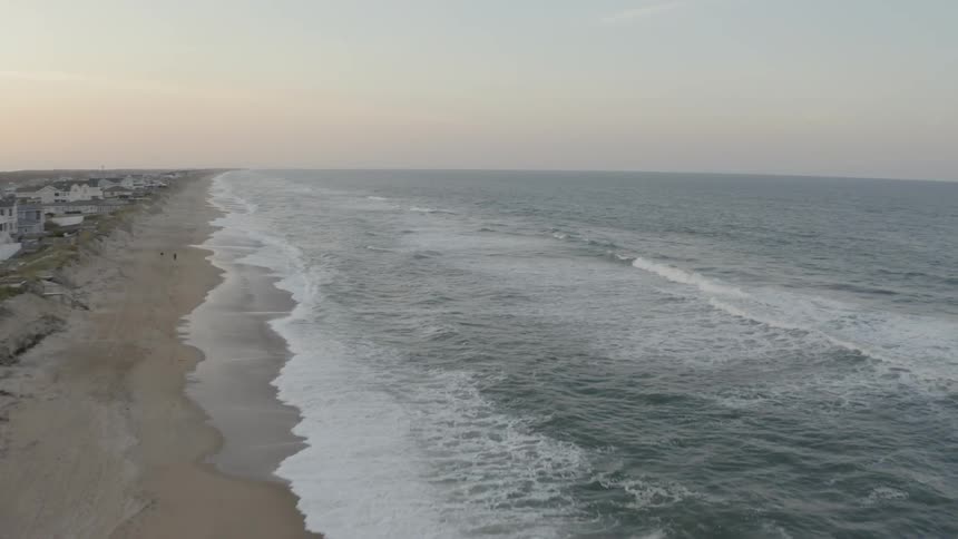 Long shoreline beach while the waves crash against beach at dusk