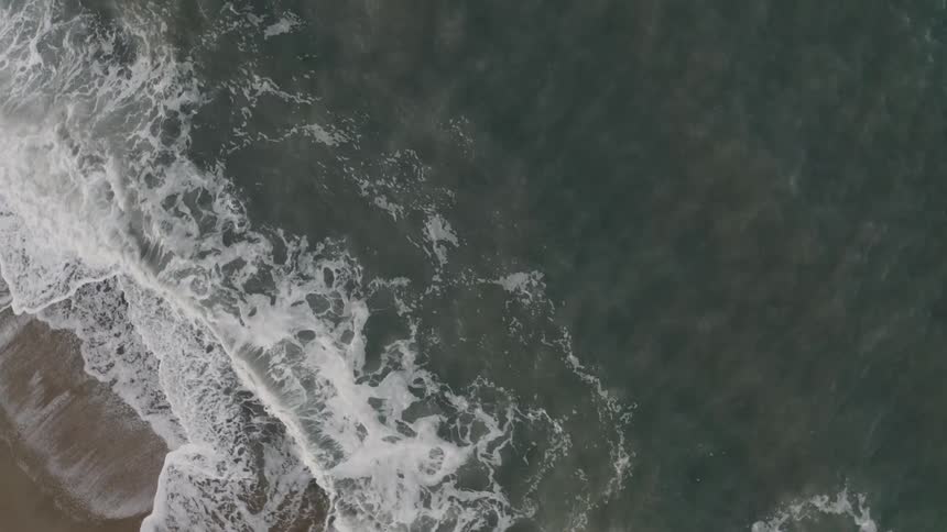 An aerial view of the ocean and waves on the sand