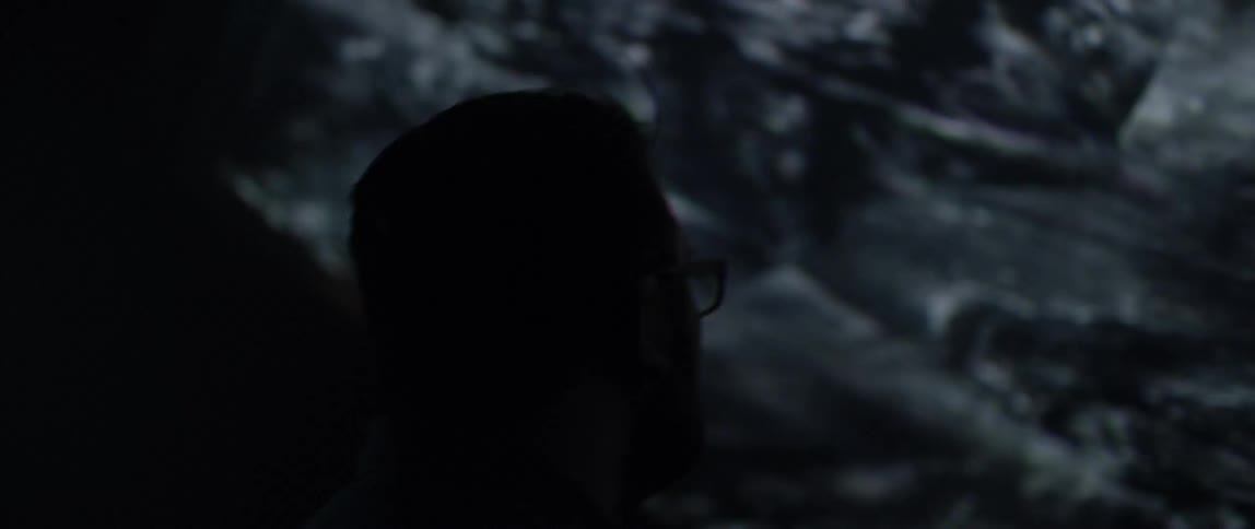 A white man watches graphics on a giant television screen