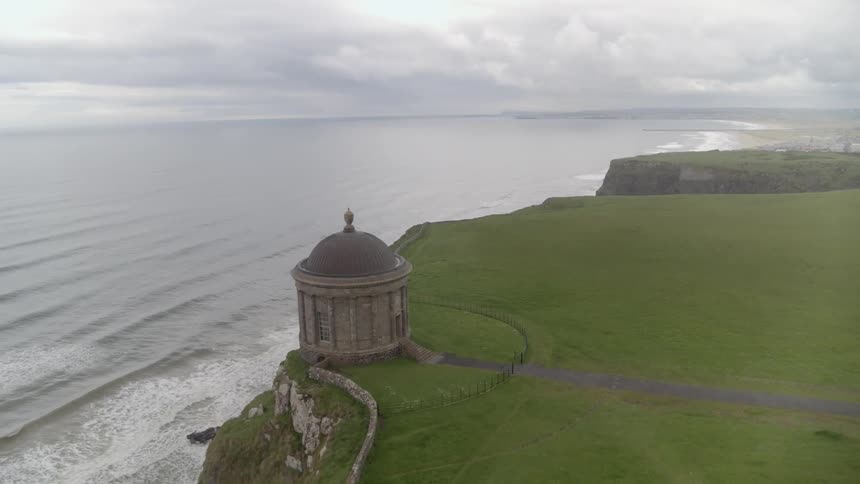 Rocky cliffs that give way to the ocean are covered in dense green grass and a rounded monument with a domed roof is built right at the edge of one of the cliffs