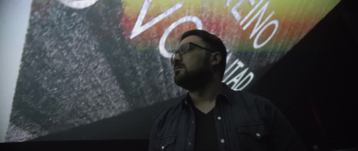 Man wearing glasses and denim looks up at words projecting onto wall