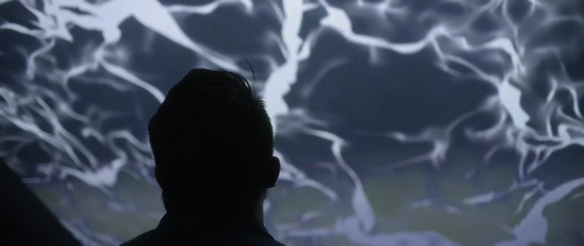 A man wearing glasses stares up at a giant video screen