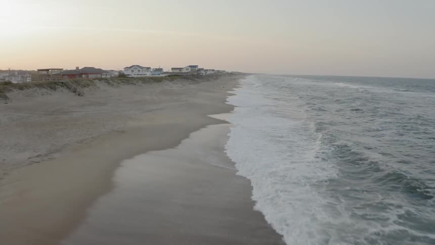 Houses lining a beach with waves crashing onshore