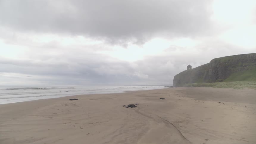 The top of a tower is visible over cliff walls on the beach where oceans waves come to a sandy shore