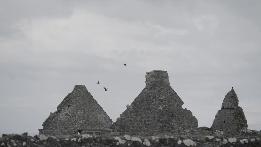 Birds fly over pyramid shaped temples and rock formations on a cloudy day