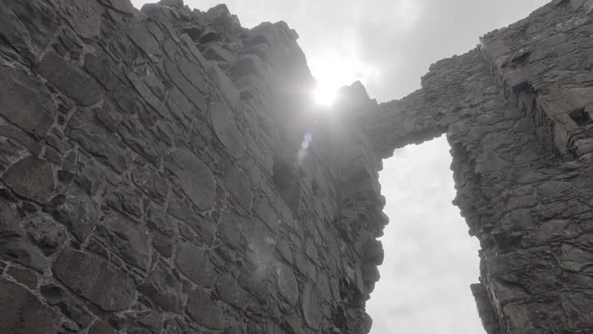 Sunlight streams through clouds onto the partially standing stone walls of the ancient dunluce castle