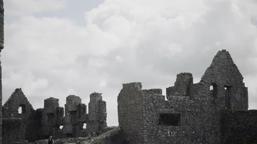 People observe the partially standing stone walls of the ancient dunluce castle on a cloudy day