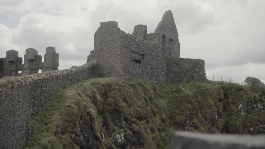 The partially standing stone walls of dunluce castle on a cloudy day