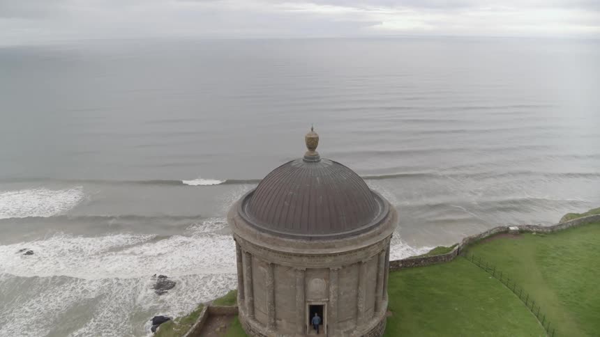 A person enters the mussenden temple while ocean waves break and splash below