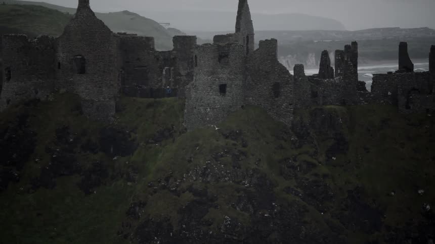 A bird flying next to an abandoned castle with the ocean in the background