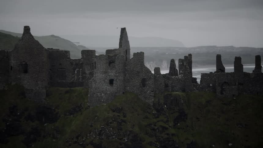 A bird flies over a broken down castle by the water