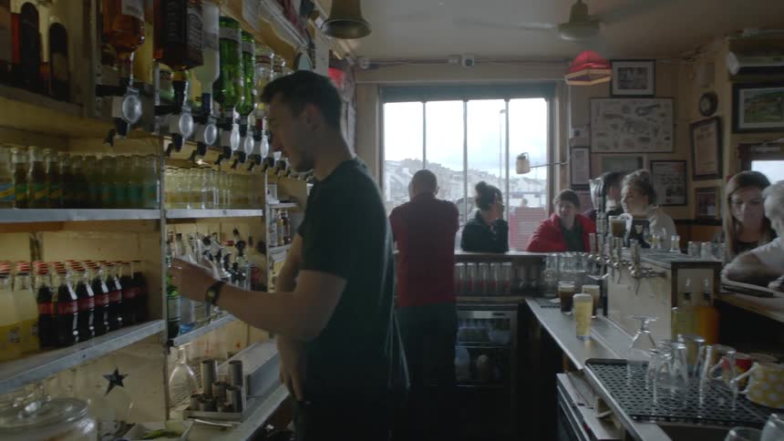 A bartender holding a glass pulls his phone out of his pocket and answers it