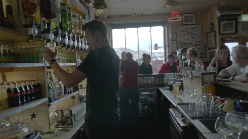 A bartender behind the bar pouring drinks for customers lining the bar