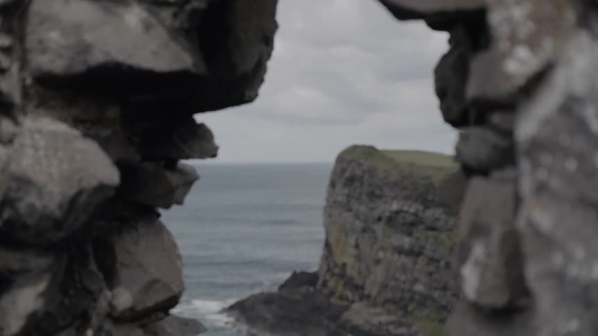 A window looking out from the slate walls of dunluce castle onto a promontory and the sea beyond