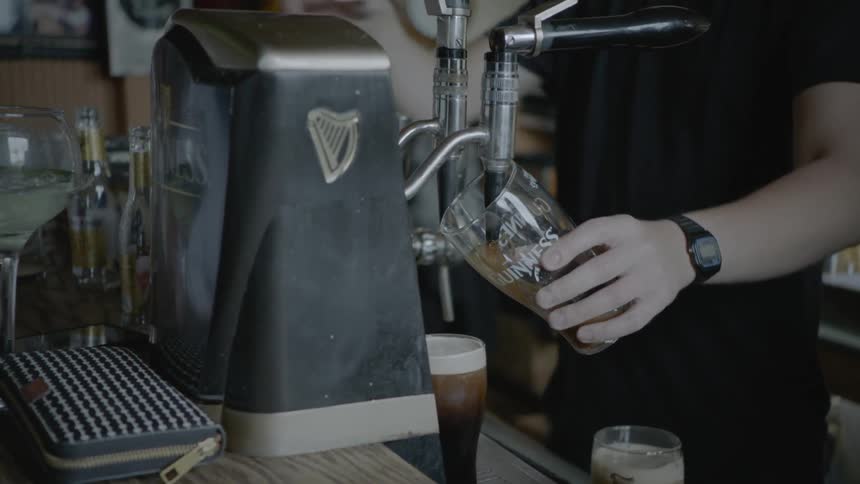 A white bartender fills a guinness pint glass with beer