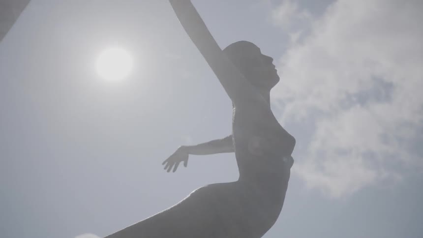 A statue of a woman with arms outstretched and bowed back in a sunny plaza