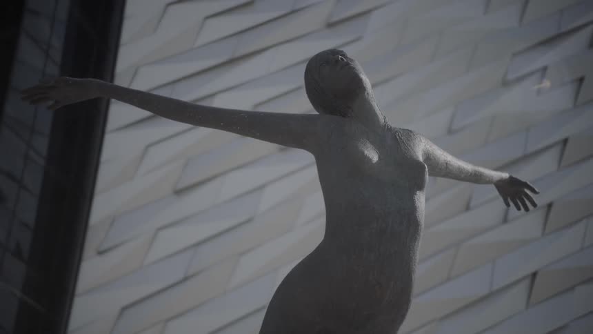 A statue of a naked woman in front of a brick wall