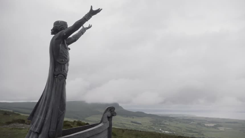 A sculpture on the top of a hill of a man rising his arms towards the heavens in the bow of a ship