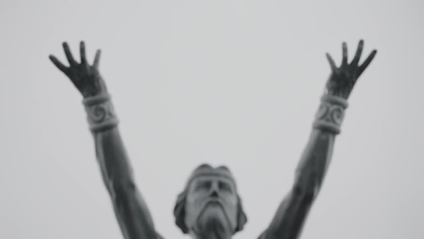 A statue of a man wearing a crown with arms raised up to the sky