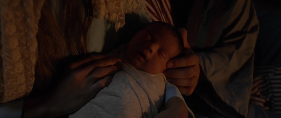 Two people holding and stroking the head of a sleeping baby