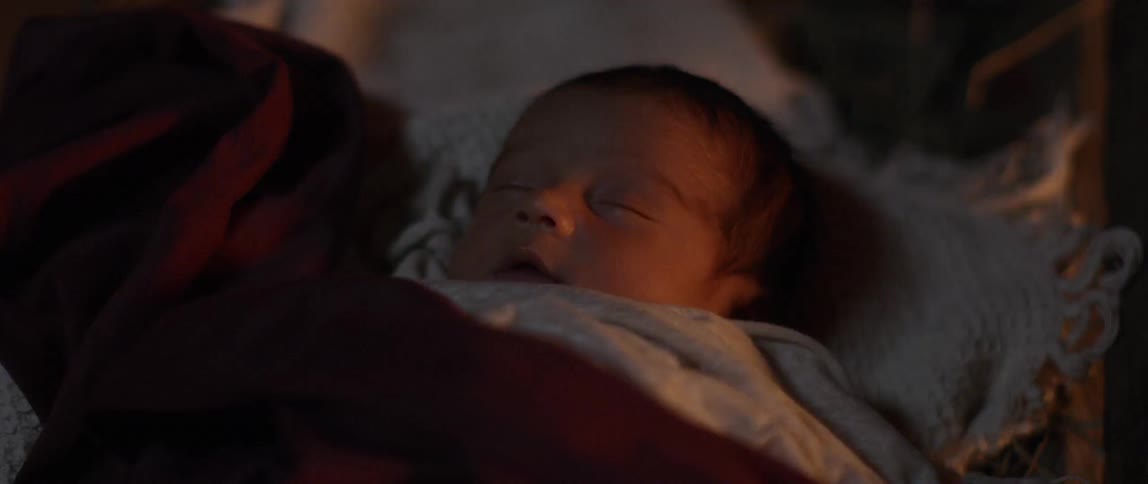 A newborn baby sleeps in a manger in a wooden building with a domestic fire