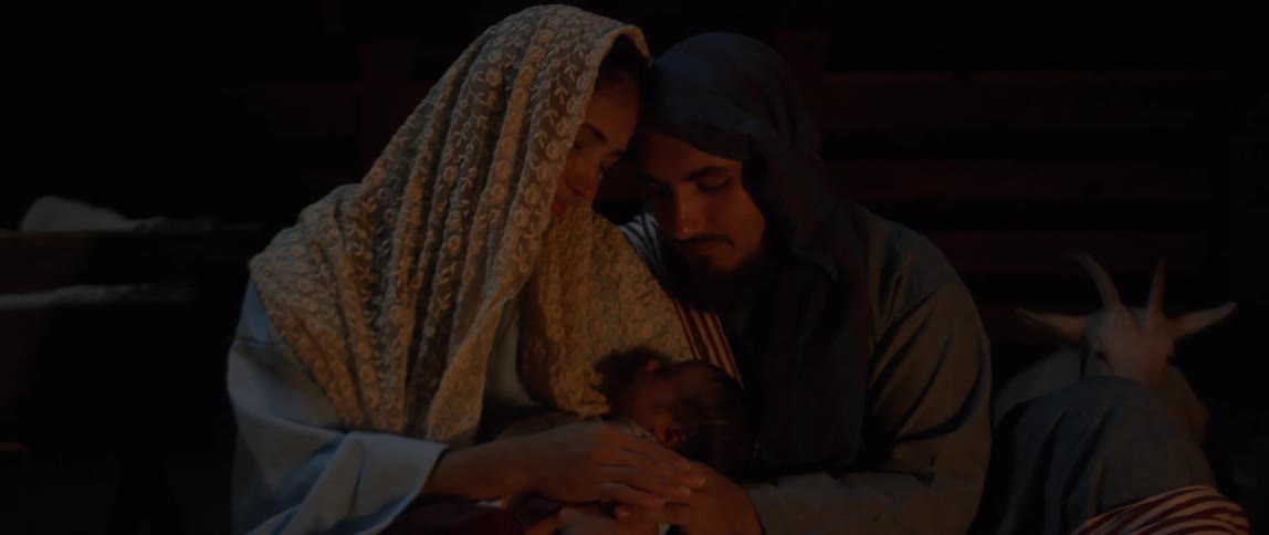 A young couple both wearing headscarves attend to a newborn baby at night